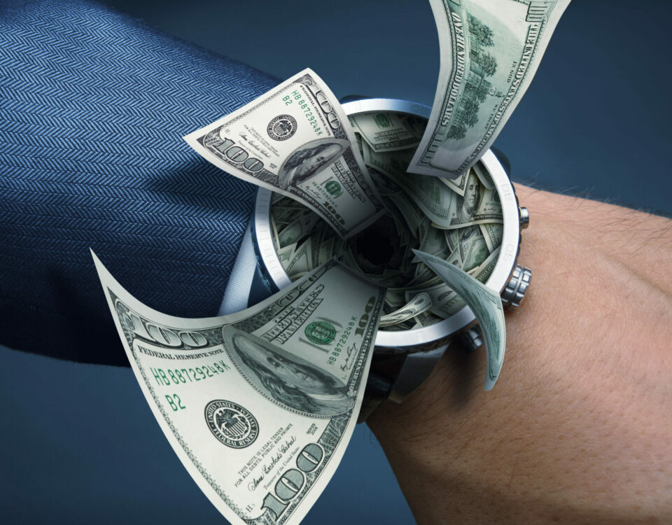 Men's hand with suit and watch with money flying out of it.