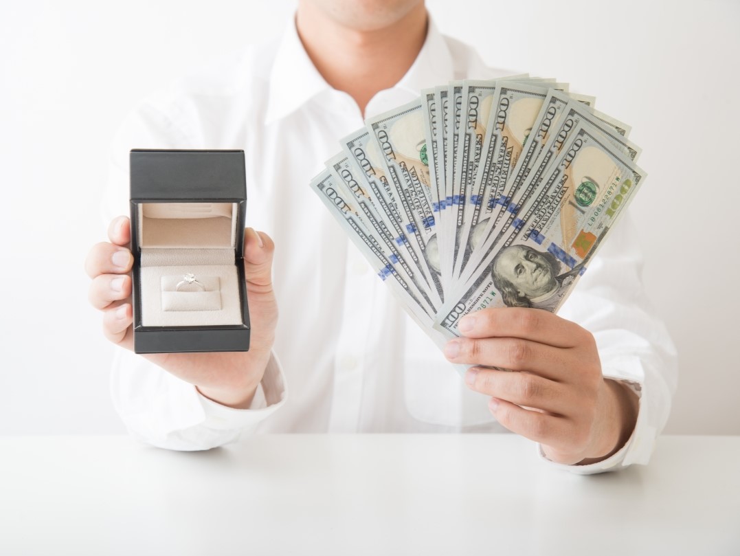 Person holding cash and an open diamond jewelry box on a table.