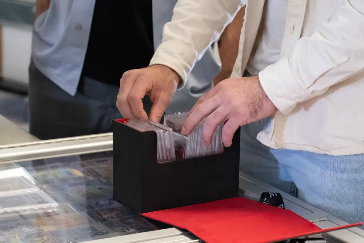 Hands selecting PSA and Beckett graded trading cards from a storage box for use as collateral on a collectible loan.