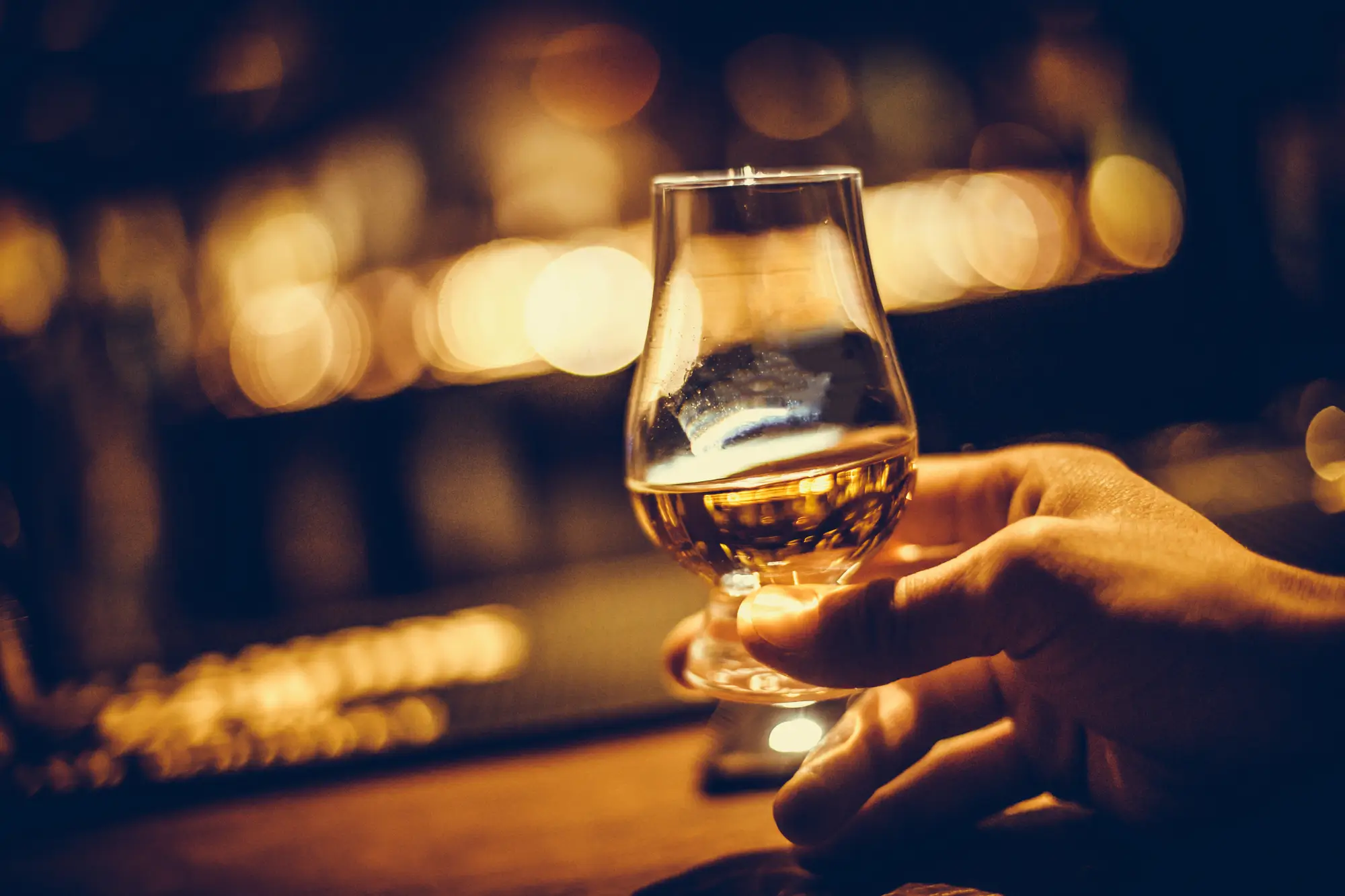 Hand holding a glass of fine whisky under warm lighting, symbolizing luxury and investment value.