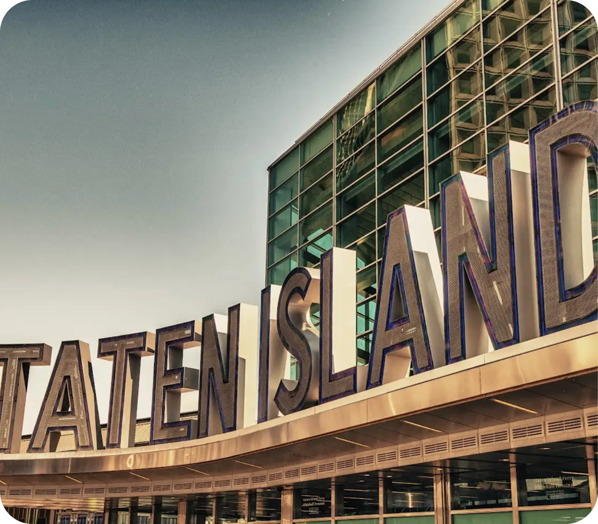 Staten Island Ferry terminal entrance in Manhattan with reflective glass facade and large illuminated signage