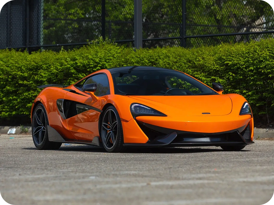 Orange McLaren 570S supercar parked outdoors with greenery in the background