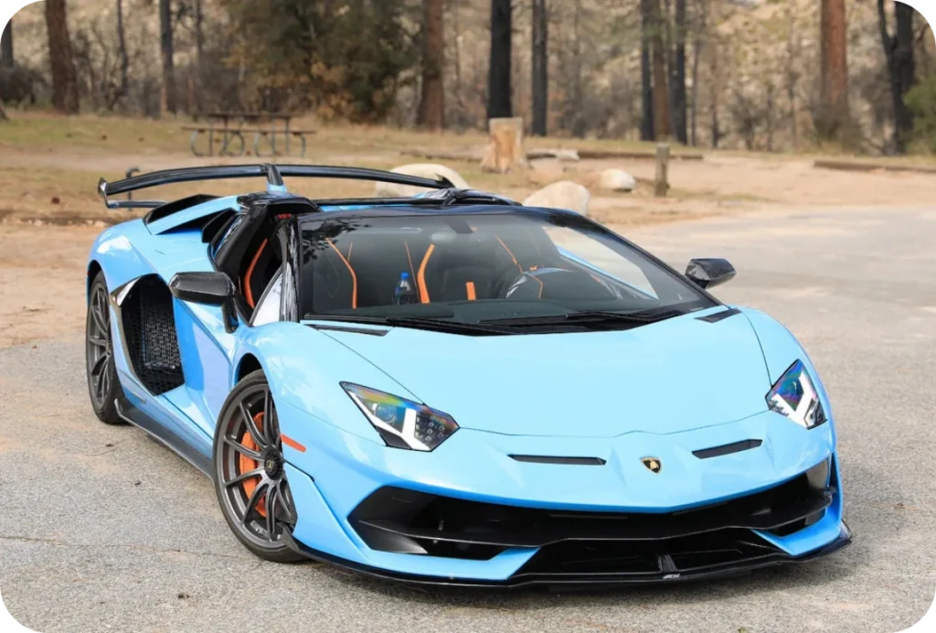 Light blue Lamborghini Aventador SVJ Roadster with orange interior accents parked in a wooded area
