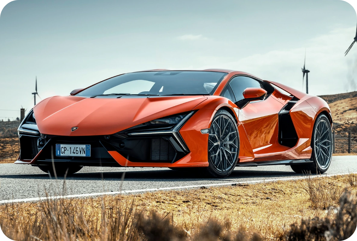Orange Lamborghini Revuelto V12 hybrid supercar parked on an open road with wind turbines in the background