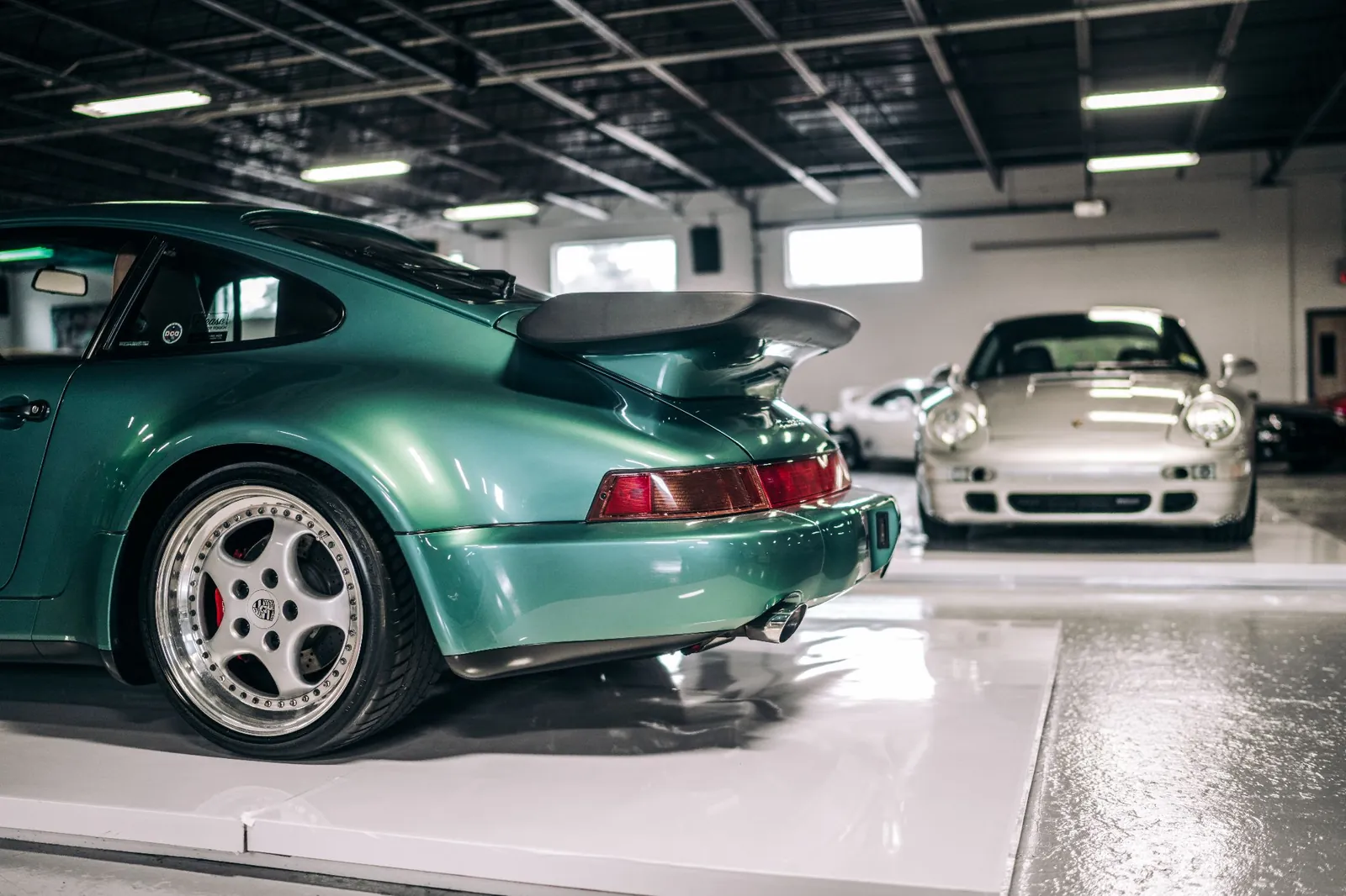 Green and silver Porsche 911s parked inside a clean, secure car storage facility
